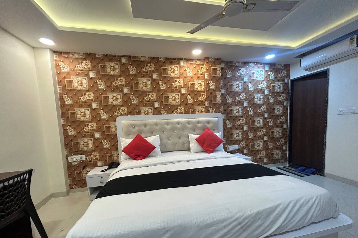 A bedroom with a tufted headboard, a bed with white bedding and red pillows, a bedside telephone, and a patterned wall.