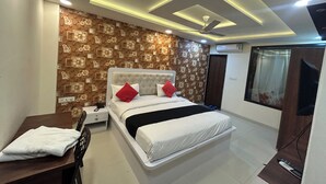 A bedroom with a bed, a desk, a chair, a ceiling fan, and a window. - Hotel Venus Inn (Indore)