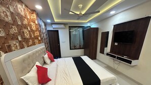 A bedroom with a bed, a TV, a ceiling fan, and a window with curtains. - Hotel Venus Inn (Indore)