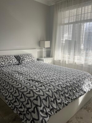 Un dormitorio con una cama grande, una mesita de noche con una lámpara y cortinas translúcidas.