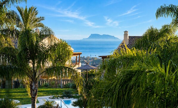 A resort with a pool, palm trees, and a view of the ocean and mountains.