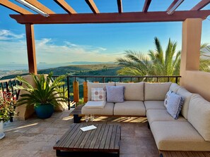 A balcony with a sofa, a wooden table, and potted plants.
