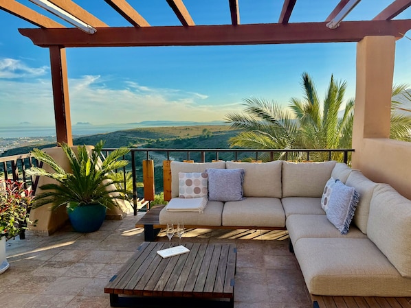 Ein Balkon mit einer Couch, einem Holztisch und Topfpflanzen.