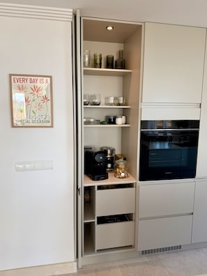 Eine moderne KĂŒche mit Einbauofen, Kaffeemaschine und einem Glas auf der ArbeitsflĂ€che.