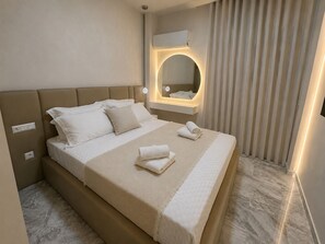 A hotel room with a large bed, a bedside table, a mirror, and a window with curtains. - Starlight Seaview Suite | Flisvos Sunset (Paleo Faliro)