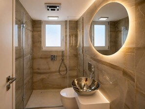 A modern bathroom with a glass-enclosed shower, a round mirror, and a stainless steel sink. - Starlight Seaview Suite | Flisvos Sunset (Paleo Faliro)