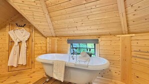 L’intérieur d’un chalet en bois, avec une baignoire, une fenêtre et un peignoir accroché au mur.