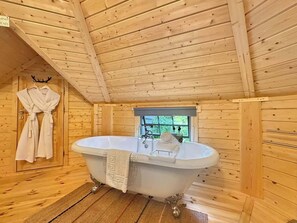 Ein Holzblockhaus-Interieur mit freistehender Badewanne, einem Fenster und einem Handtuchhalter.