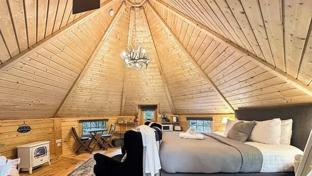 Une chambre mansardée chaleureuse, avec un lit, une chaise, une petite table et un ventilateur de plafond.