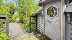 A wooden deck leading to a grey building with a hexagonal window. - Willow Lodge at Aos Sí (Ballachulish)