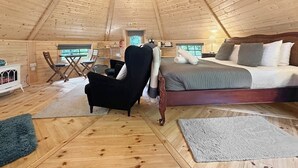A cozy cabin interior with a bed, a chair, a table, and a chandelier. - Willow Lodge at Aos Sí (Ballachulish)
