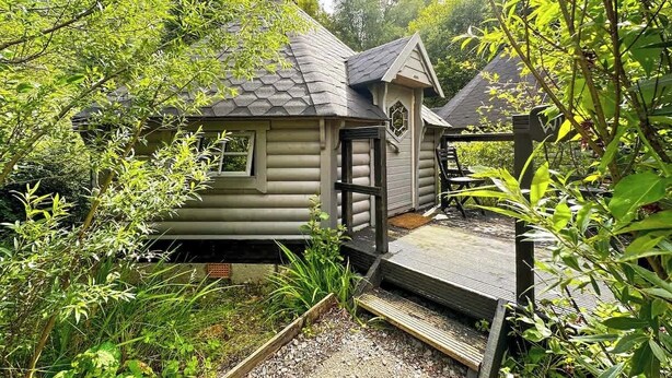 A log cabin with a small porch and a covered deck area. - Willow Lodge at Aos Sí (Ballachulish)