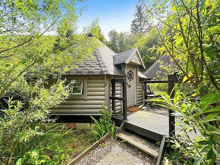 A rustic cabin with a small porch, surrounded by dense greenery.. Willow Lodge at Aos Sí
