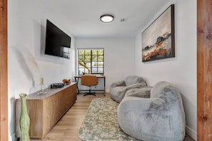 A modern living room with a wooden cabinet, a TV, a desk, and a large window. - Scottsdale Burro! Resort Pool, Casita & Putting (Scottsdale)