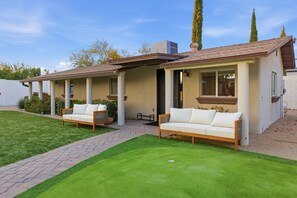 Ein Wohnhaus mit überdachter Terrasse, zwei Sofas und einem gepflegten Rasen.