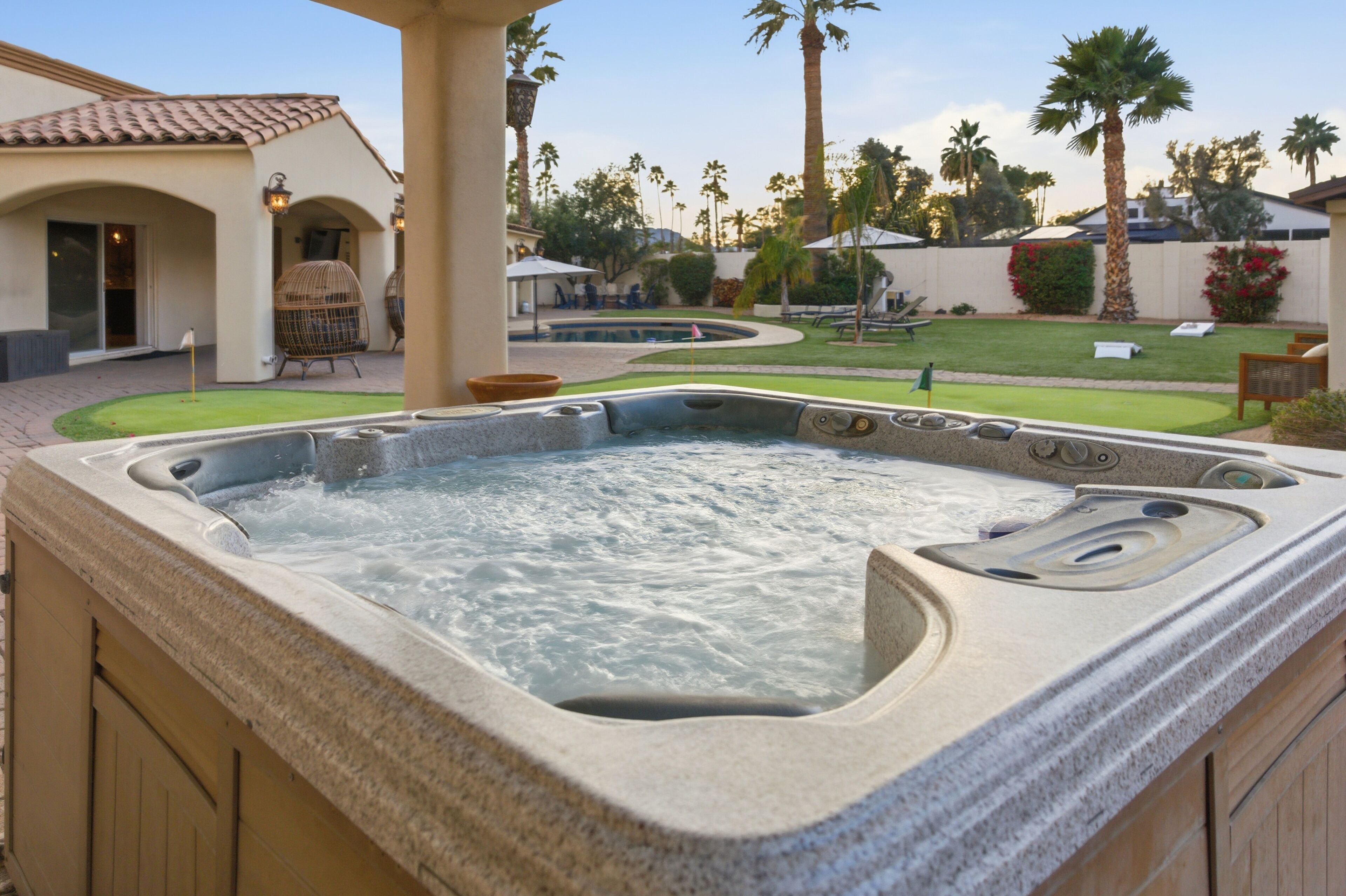 Un jacuzzi dans un jardin, avec une terrasse, des palmiers et une piscine.