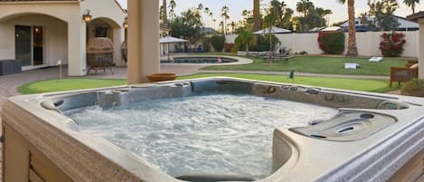 Un jacuzzi dans un jardin, avec une terrasse, des palmiers et une piscine.