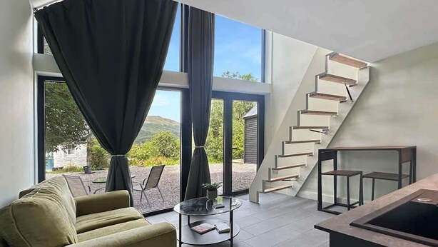 Ein modernes Wohnzimmer mit einer Couch, einem Glastisch und einer Treppe, die zu einer oberen Etage führt.