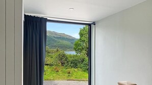 Ein Zimmer mit großem Fenster, Holzboden und Blick auf einen See und Hügel.