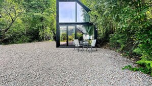Ein modernes, zweistöckiges Haus mit Glasfassade, einem Schotterweg und einer Sitzgelegenheit im Freien.