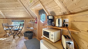 A compact wooden cabin with a dining area, kitchenette, and a window with a view. - Birch Lodge at Aos Sí (Ballachulish)