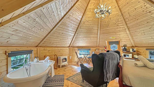 A wooden cabin interior with a bathtub, a bed, a fireplace, and a dining area. - Birch Lodge at Aos Sí (Ballachulish)