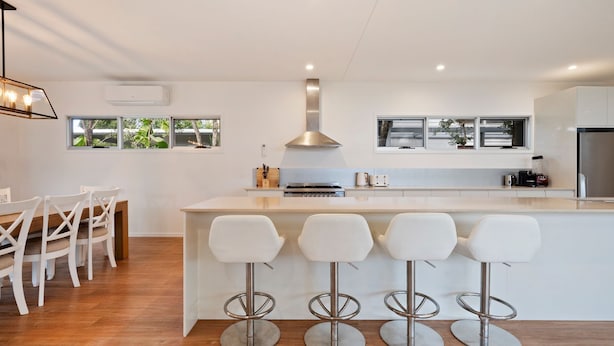 Een moderne keuken met een centraal eiland, barkrukken, een fornuis en een groot raam.