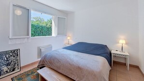 A bedroom with a bed, two bedside lamps, a window, a radiator, and a framed picture on the wall. - Les Mouettes by Interhome (Soustons)