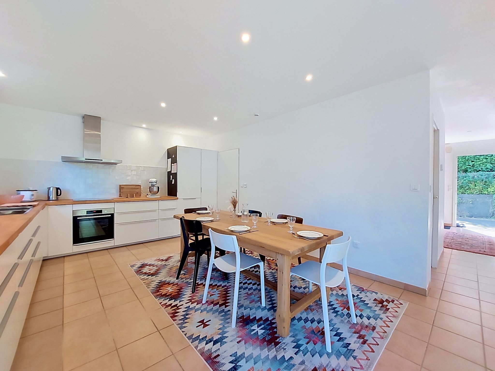 A modern kitchen with white cabinets, a wooden dining table, and a patterned rug.