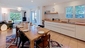 A modern kitchen with a dining area, large windows, and a view of greenery. - Les Mouettes by Interhome (Soustons)