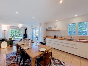 A modern kitchen with a dining area, large windows, and a view of greenery. - Les Mouettes by Interhome (Soustons)