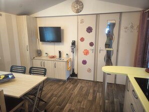 Een compacte kamer met een flatscreen televisie, een houten kast, een eettafel met stoelen, een kleine kitchenette en een deur versierd met decoratieve stickers.