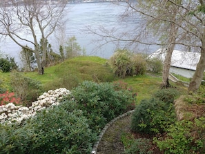 A landscaped garden with a variety of plants and shrubs, a stone pathway, and a view of a body of water. - 6-bedroom luxurious house in Vestland for your getaway to the fjords of Norway (Vestland)