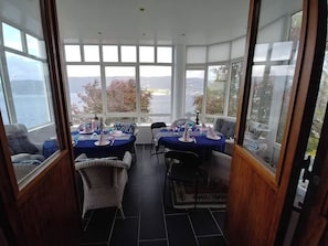 A dining area with tables set for four, large windows with a view of the sea, and a high ceiling. - 6-bedroom luxurious house in Vestland for your getaway to the fjords of Norway (Vestland)