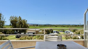 Ein Balkon mit Tisch und Stühlen, mit Blick auf einen Campingplatz mit Wohnmobilen und einem klaren Himmel.