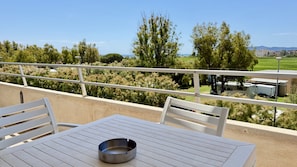 Ein Balkon mit Tisch und Stühlen, einer Metallschale und Blick auf Bäume sowie entfernte Gebäude.