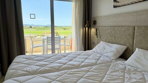 Ein Hotelzimmer mit Bett, Blick auf eine grüne Landschaft und einem Tisch mit Stühlen draußen.