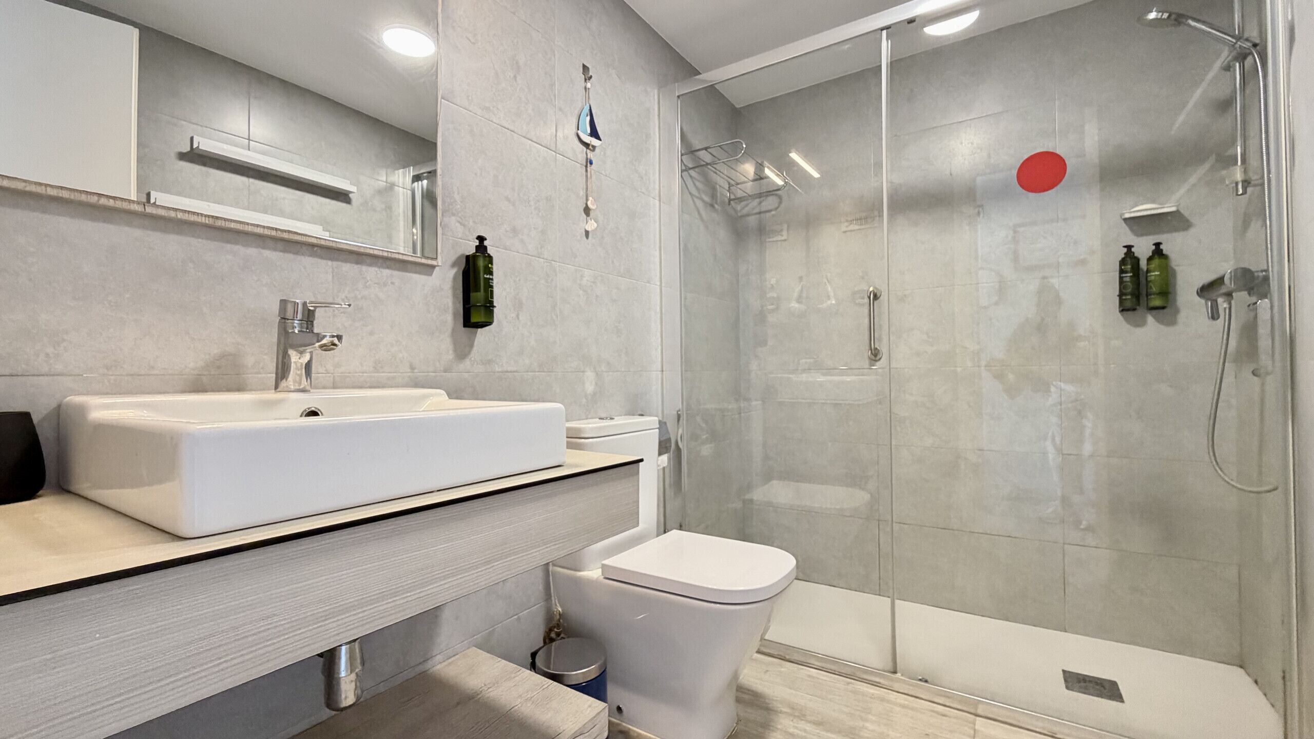 A modern bathroom with a white sink, toilet, and glass shower enclosure.