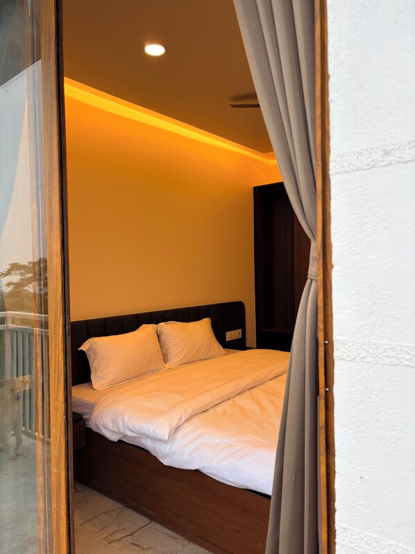 A bedroom with a wooden headboard, white bedding, and a visible power outlet.