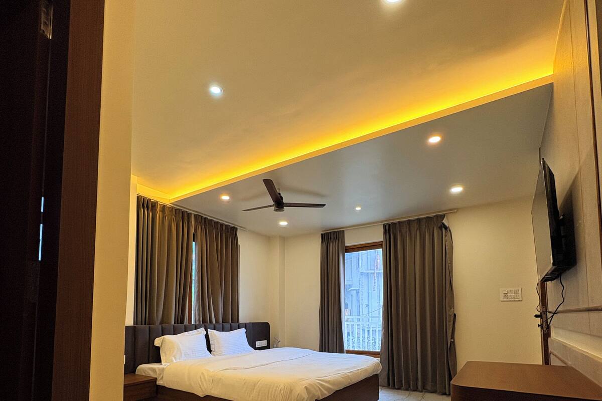 Una habitación de hotel moderna con una cama grande, ventilador de techo y televisor montado en la pared.