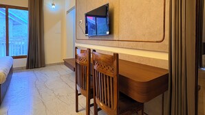 Una habitación moderna con techo de madera, televisor montado en la pared, escritorio con sillas y un ventanal con cortinas.