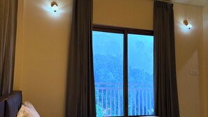 Habitación de hotel con una cama grande, dos ventanas con cortinas, techo de madera y vistas a un balcón.