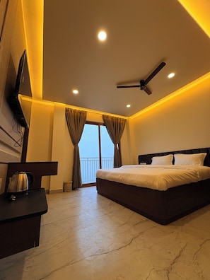 A hotel room with a bed, a ceiling fan, a TV mounted on the wall, and a balcony with curtains.