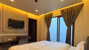 Habitación de hotel con cama, televisor de pantalla plana montado en la pared, ventilador de techo y ventana con cortinas.