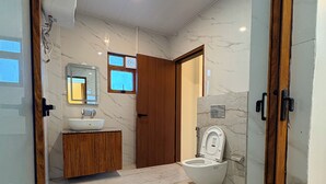Un baño con suelo de mármol, puerta de madera, lavabo blanco y un inodoro.