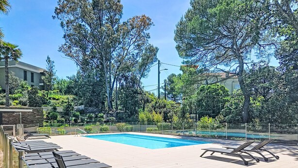 Ein Pool mit Liegestühlen, umgeben von Bäumen und einer Steinmauer.