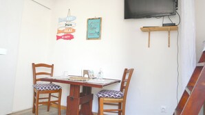 Zona pranzo con due sedie in legno, un tavolo, una televisione montata a parete e una piccola mensola sotto.