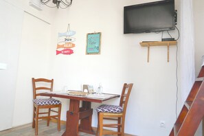 A dining area with two wooden chairs, a table, a television mounted on the wall, and a small shelf below it. - Studio with terrace Port de St Goustan (Auray)