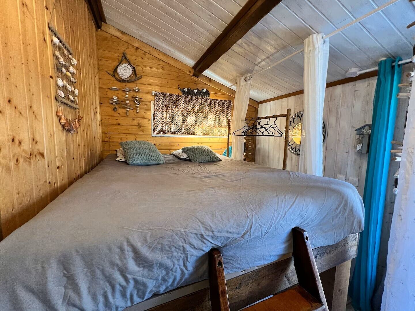 A wooden cabin bedroom with a bed, pillows, wall decor, and a window with curtains.