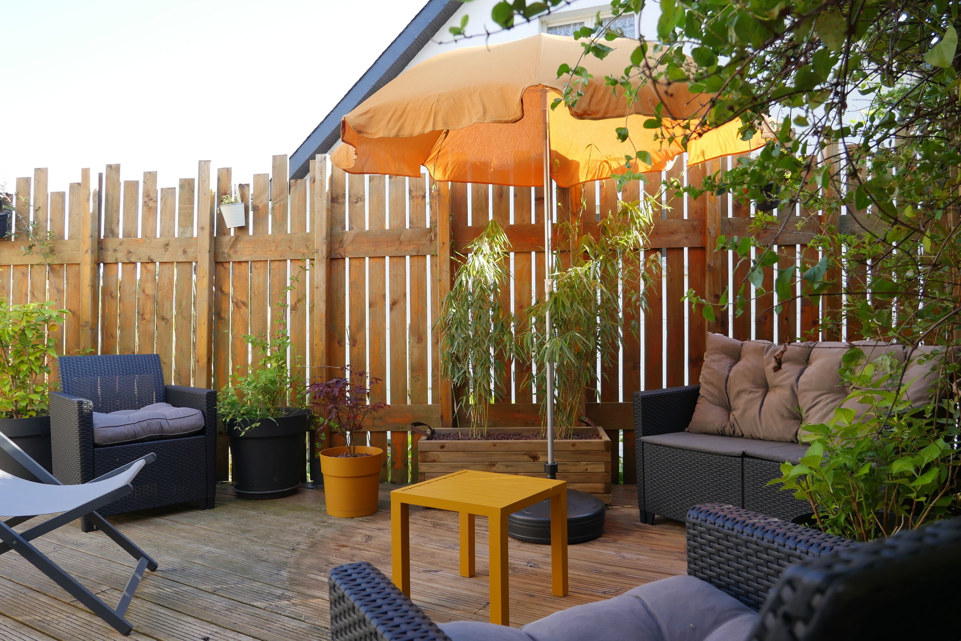 An outdoor patio with wicker furniture, a yellow table, and potted plants.
